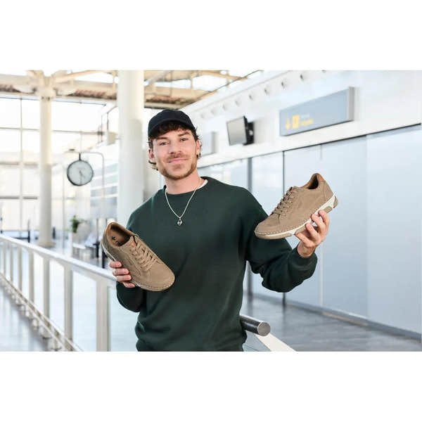 Man holding tan leather lace-up shoes, wide fit, casual style, in an airport terminal.