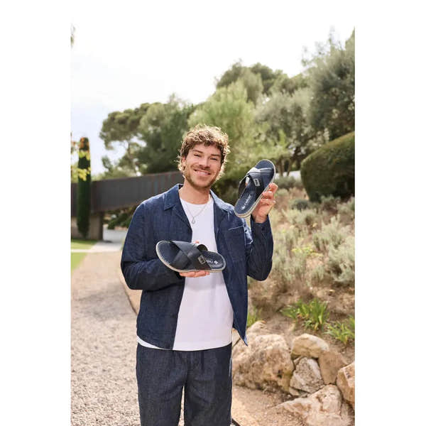 Man holding Rieker 21082-14 men's wide navy/grey leather elasticated mules, outdoor background, casual footwear.