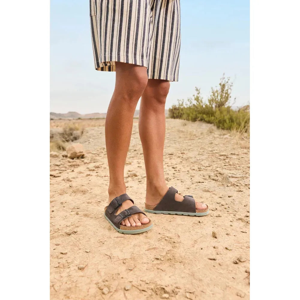 Rieker men's wide fit grey suede buckle mule sandals on sandy desert ground.