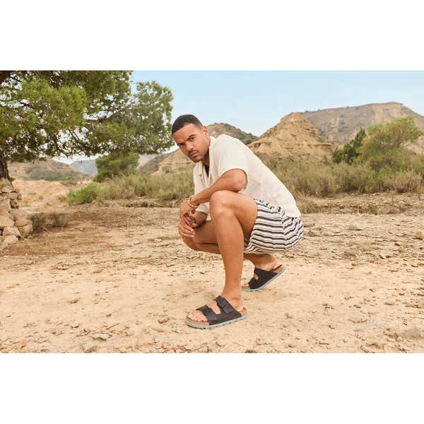 Rieker 21190-45 men's wide-fit grey suede buckle slip-on mules in an outdoor desert setting.
