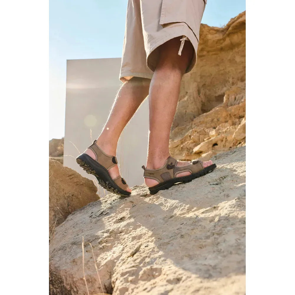 Rieker 25055-64 men's wide fit stone touch fastening sandals on rocky terrain, outdoor summer footwear with adjustable straps.