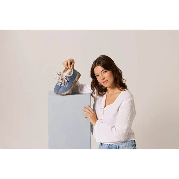 Woman holds light blue lace-up shoes with beige soles, casual style, made of textile material, against a pale background.