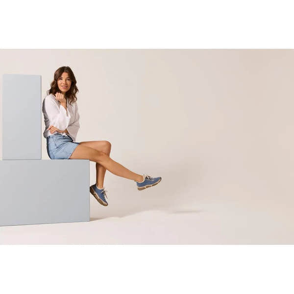 Light blue lace-up shoes with a chunky sole, worn by a woman sitting on geometric blocks against a neutral background.
