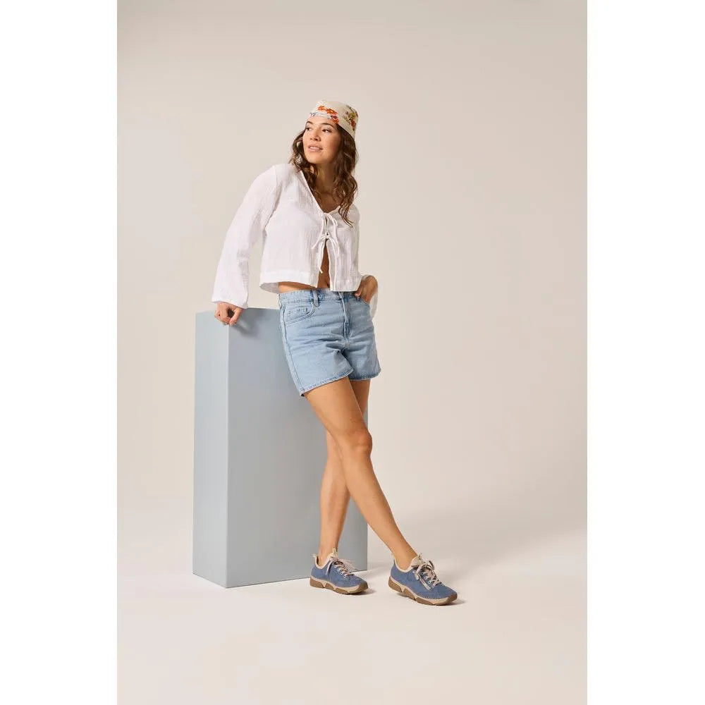 Light blue lace-up shoes with beige sole, worn by woman in casual white top, denim shorts, and colorful hat.