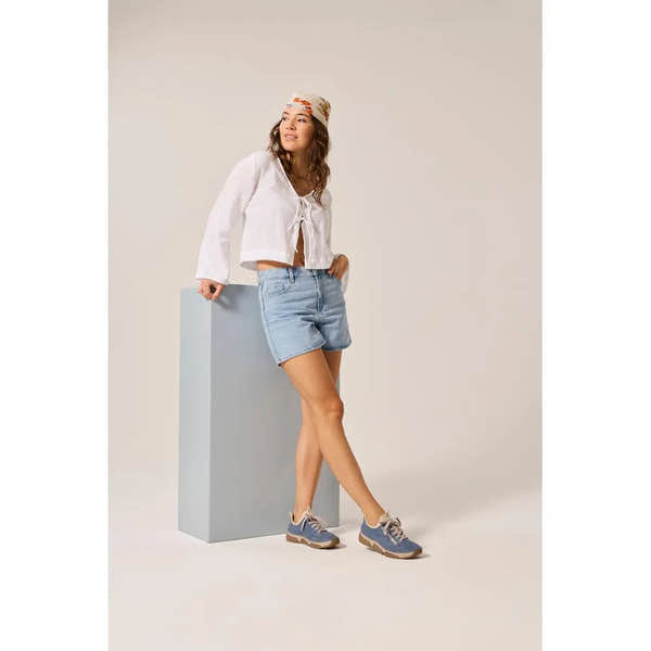 Light blue lace-up shoes with beige sole, worn by woman in casual white top, denim shorts, and colorful hat.