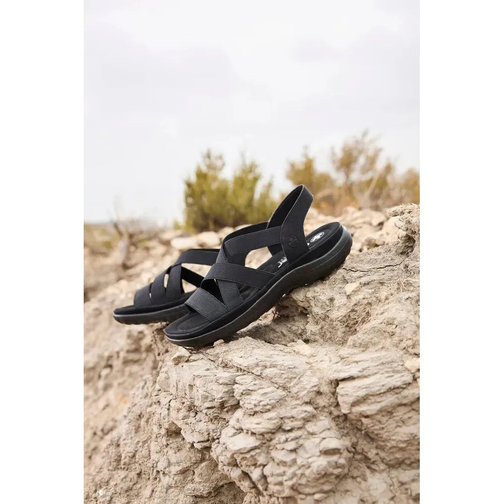 Rieker 64857-00 Ladies Black Elasticated Sandals on rocky terrain, open toe, adjustable straps, lightweight comfort footwear.