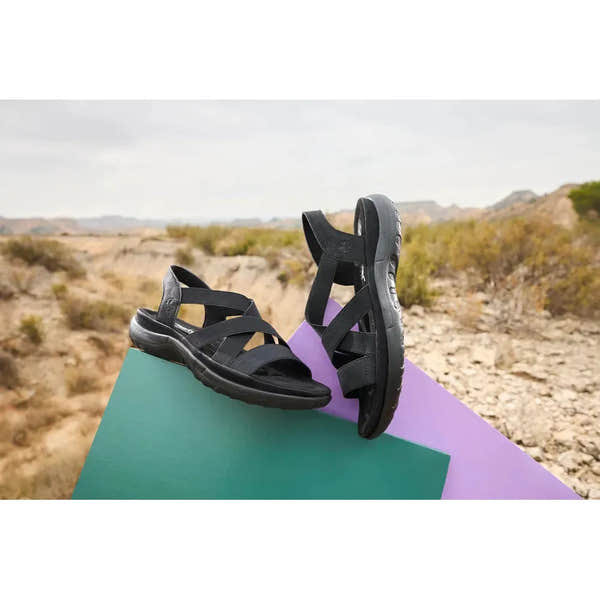 Rieker 64857-00 women's black elasticated sandals, open-toe design with adjustable straps and cushioned sole, outdoor setting.