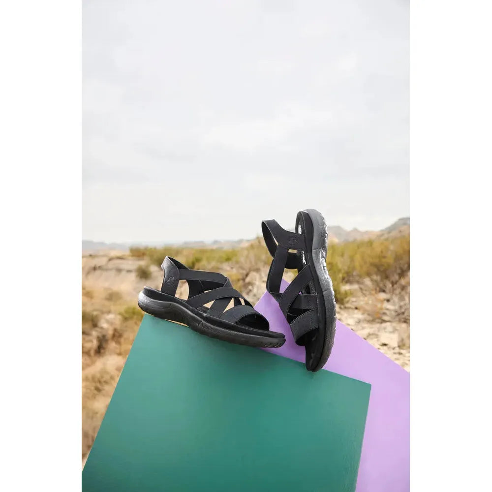 Rieker 64857-00 women’s black elasticated slip-on sandals with cushioned soles, outdoor setting.