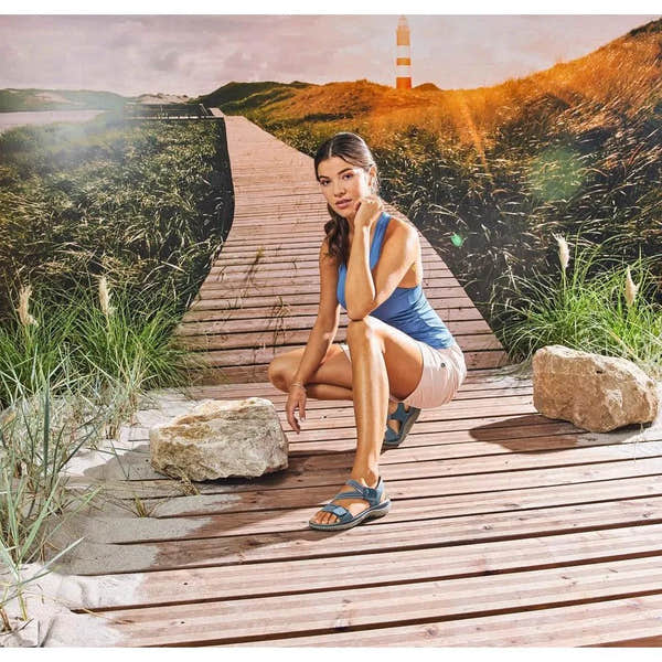 Rieker 64870-14 women's blue Touch fastening sandals on a wooden boardwalk with rocks, grass, and lighthouse background.