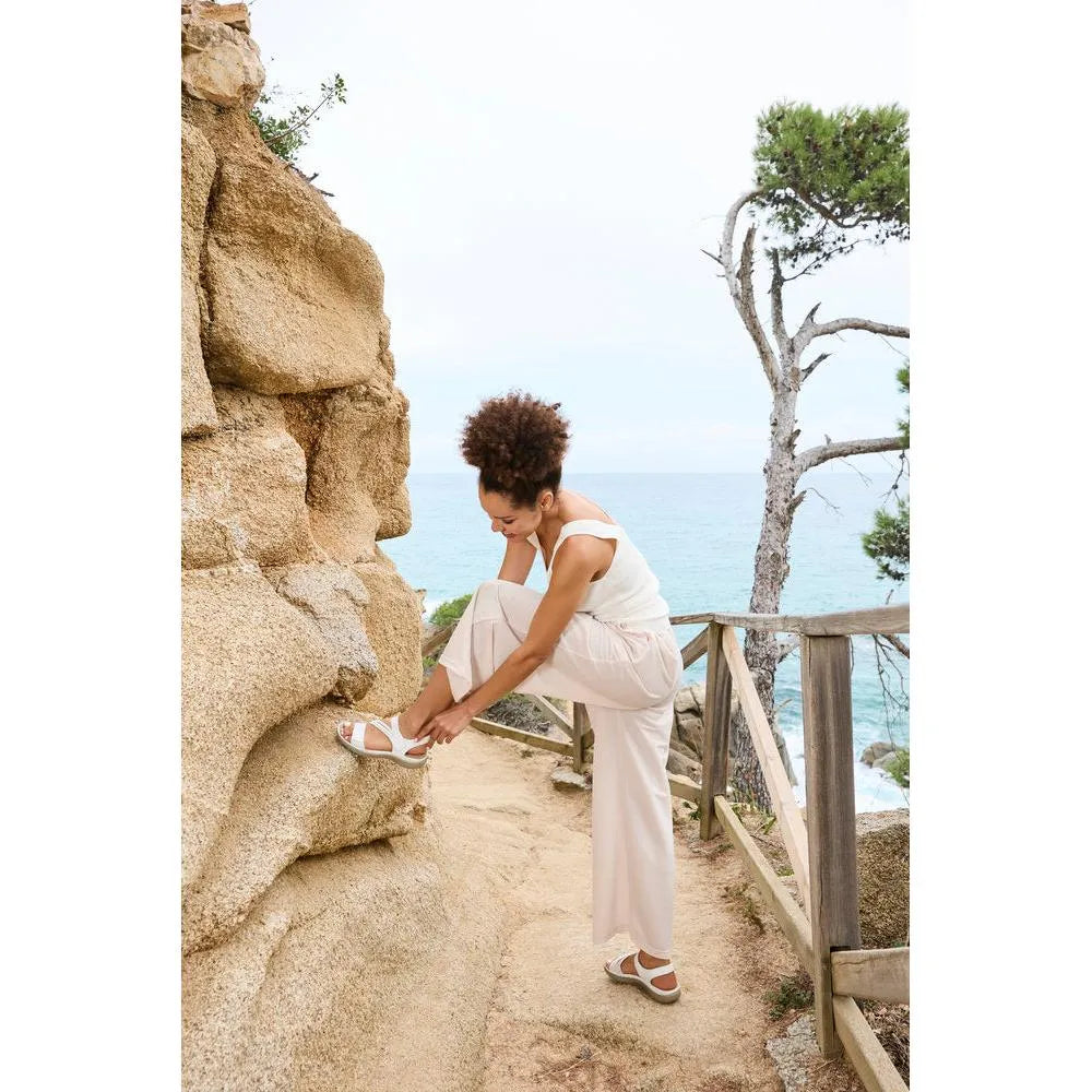 Women's white touch fastening sandals with open toe and cushioned sole by Rieker, worn by woman outdoors near the sea.