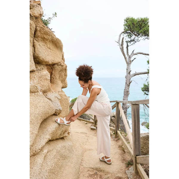 Women's white touch fastening sandals with open toe and cushioned sole by Rieker, worn by woman outdoors near the sea.