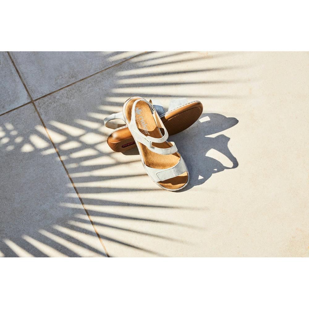 Rieker 659C7-93 women's silver leather touch fastening sandals on tiled floor with shadow patterns.