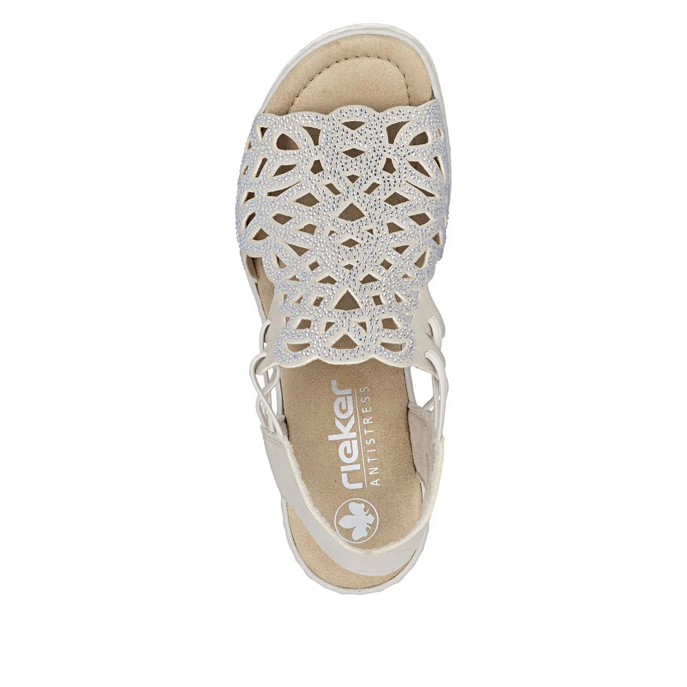 Rieker 67465-62 ladies beige elasticated slip-on sandal with intricate cutout design and embedded rhinestones.