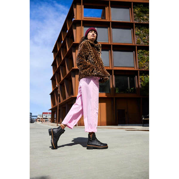 Women wearing Rieker 72617-00 black ankle boots with lace-up and zip closure, paired with pink pants and leopard print jacket outdoors.