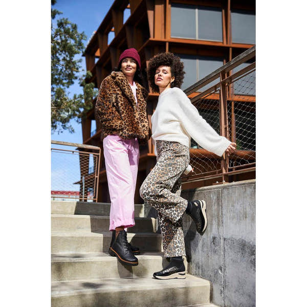 Rieker 72617-00 women's black ankle boots with zip and lace details, styled with leopard-print pants on outdoor stairs.