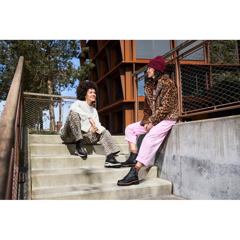 Rieker 72617-00 women's black zip and lace ankle boots with chunky sole, worn by two women in trendy animal print and casual outfits.