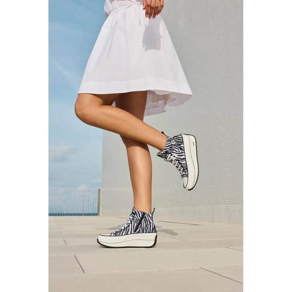 Zebra-print vegan ankle boots with zipper and lace, platform sole, worn by a person in a white dress outdoors.