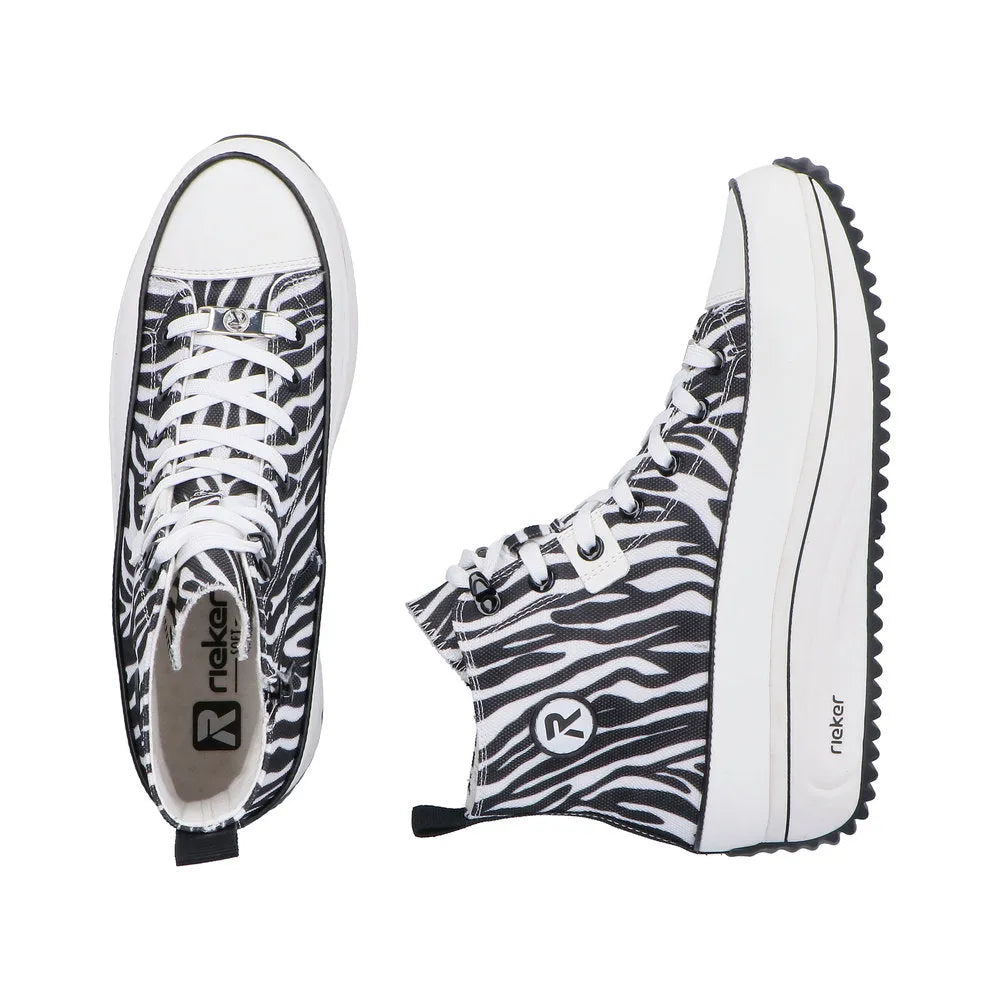 Black and white zebra-textile vegan ankle boots with zip and lace, chunky white sole, and Rieker branding.