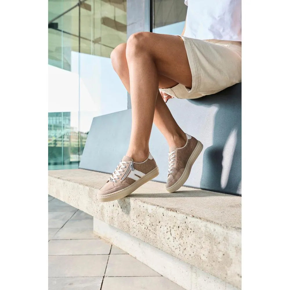 Woman sitting outdoors wearing beige suede zip and lace shoes with white accents and a thick sole.