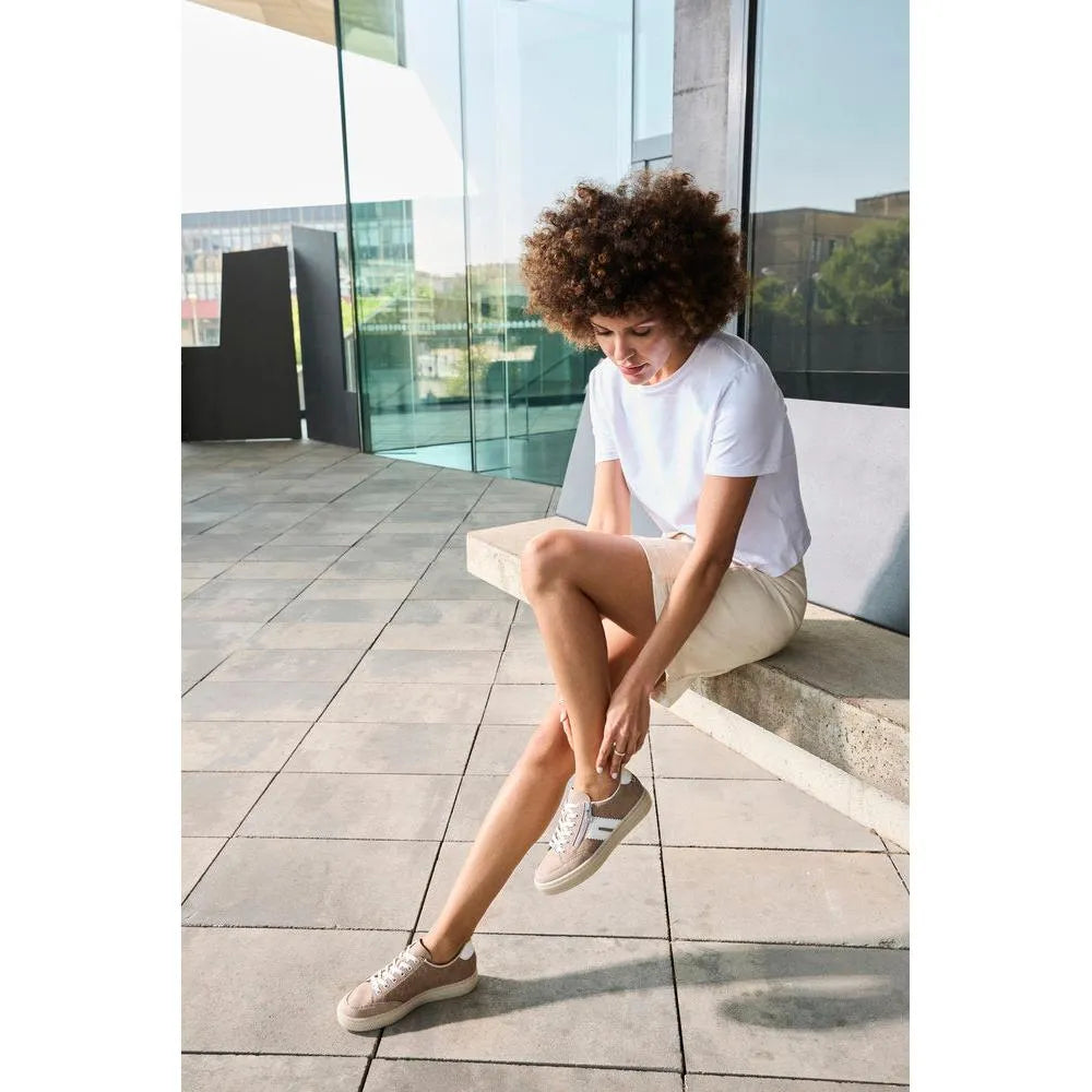 Women wearing beige suede Rieker L5903-20 shoes with zip and lace details, sitting on a bench outside.