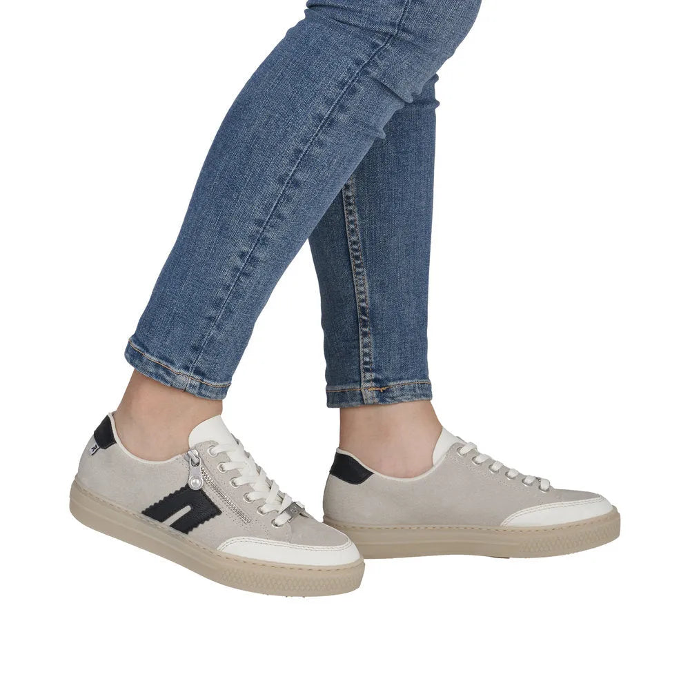 Rieker L5903-40 women's off-white suede sneakers with zip, lace-up design, and beige soles, paired with blue jeans.