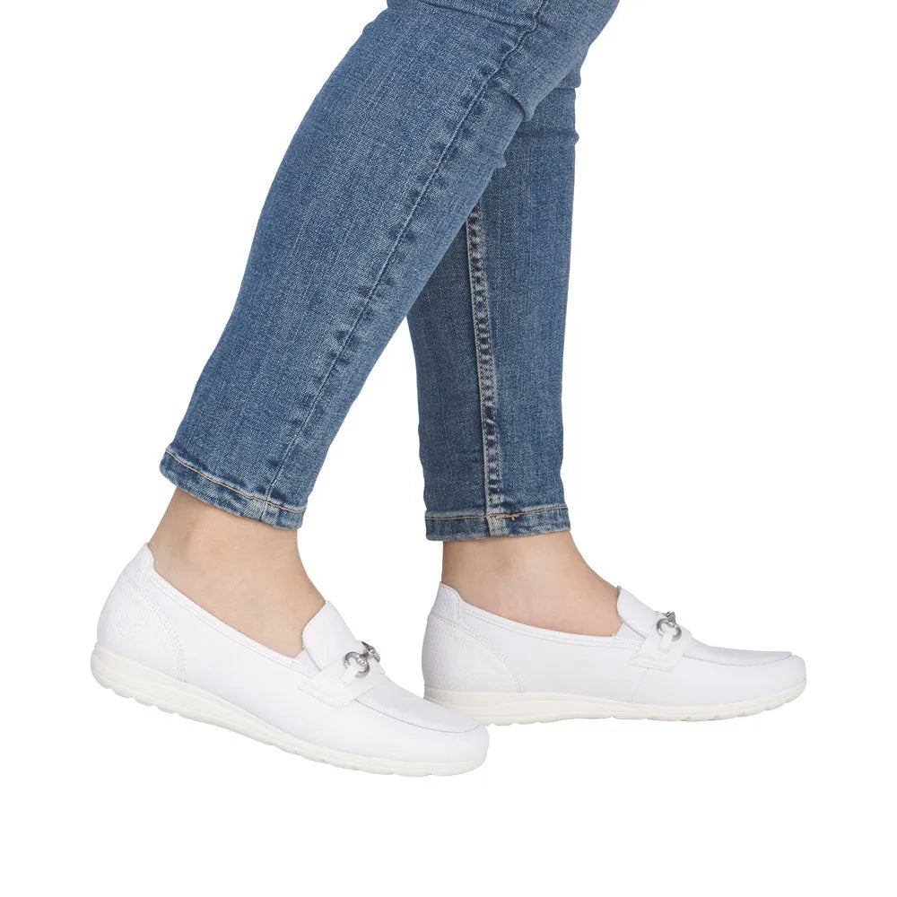 Women’s white leather slip-on shoes with silver chain detail, paired with blue jeans.