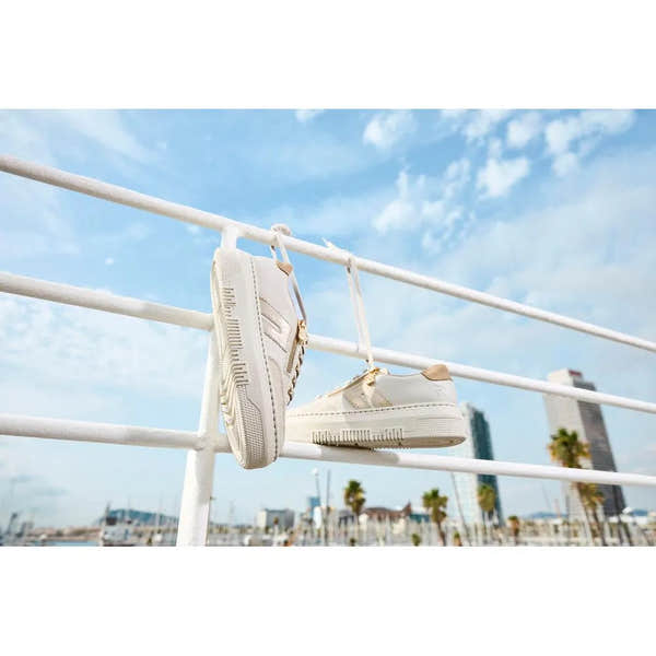 Off-white leather trainers with zip and lace, on a white railing against a blue sky and cityscape background.