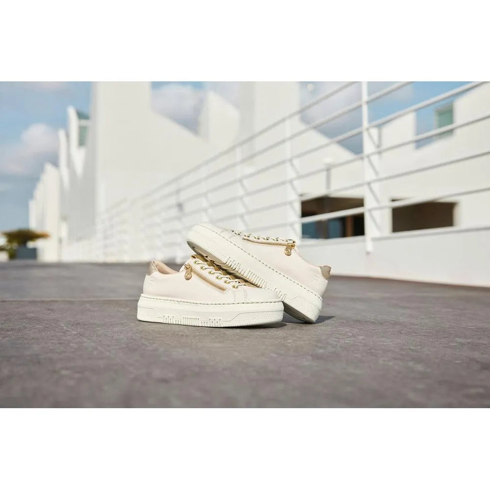 Off-white patent trainer shoes with side zips and chunky soles, styled for ladies, outdoors on a paved surface.