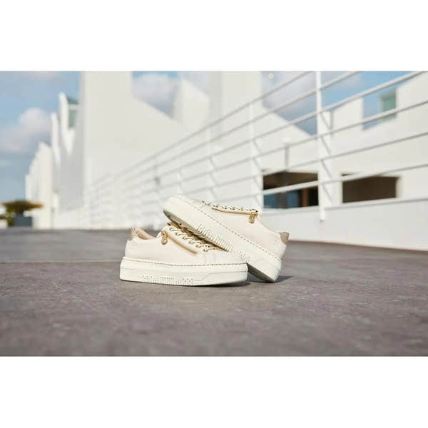 Off-white patent trainer shoes with side zips and chunky soles, styled for ladies, outdoors on a paved surface.