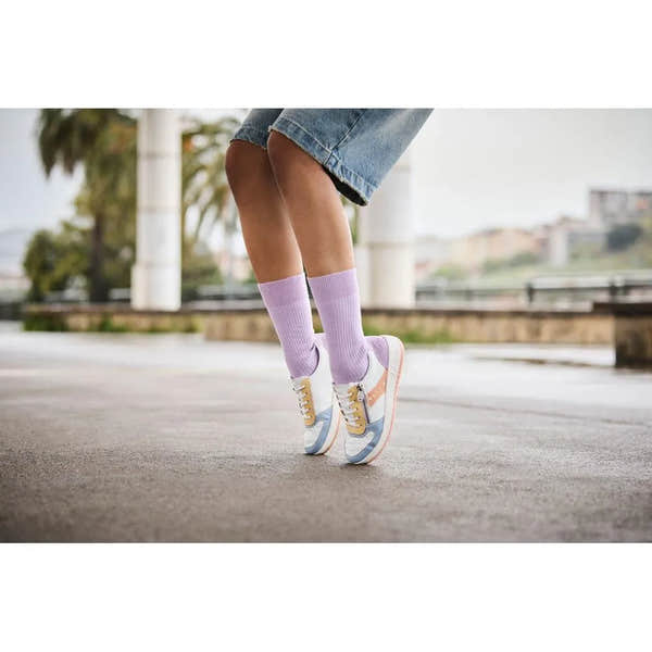Rieker M5520-91 women's multi-zip and lace trainers with pastel color accents, worn with purple socks, outdoor urban setting.
