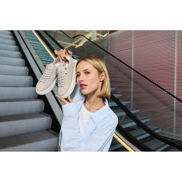 Woman holding off-white suede zip and lace shoes, casual style, in modern urban setting.