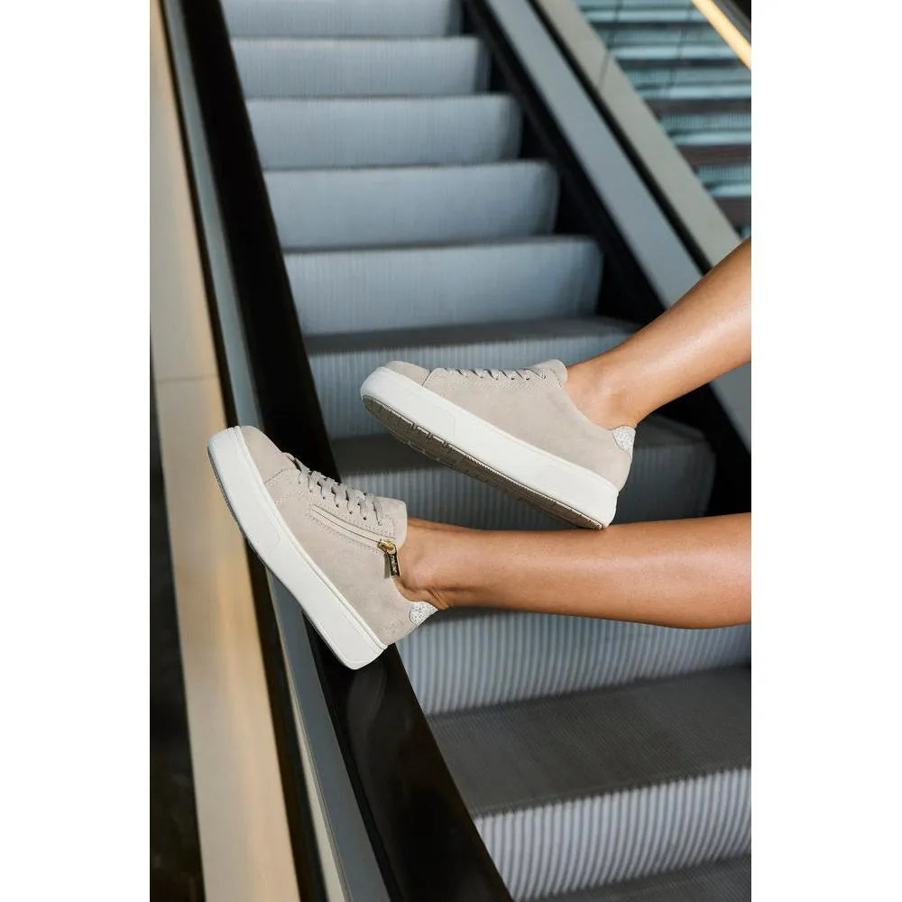 Off-white suede zip and lace women's sneakers on an escalator step, with a thick white sole and subtle textured detail.