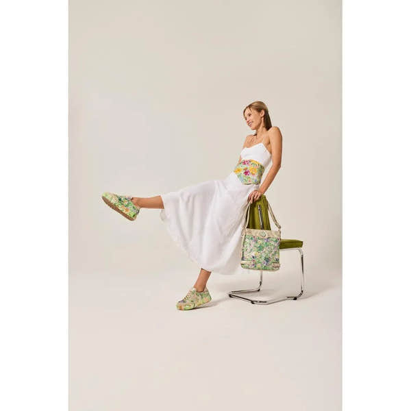 Ladies white dress with colorful floral side zip trainers, holding a floral bag, sitting on a chair.