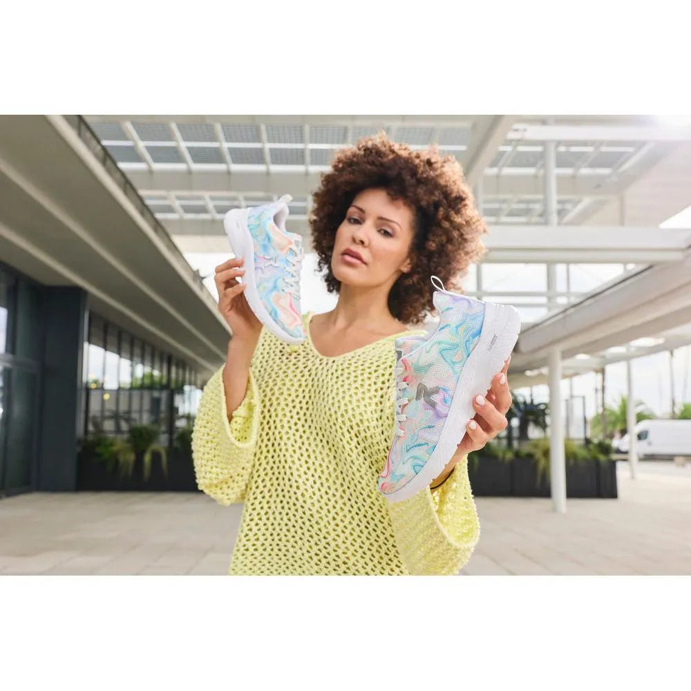 Woman holding colorful mesh vegan lace-up trainers, casual style, pastel swirls, white soles, in modern architectural setting.