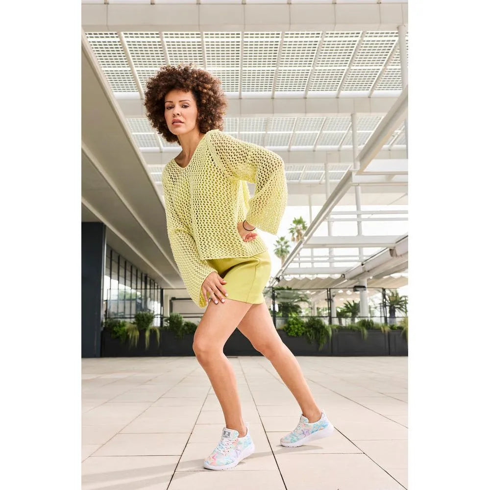 Rieker M8500-90 vegan lace-up trainers in multi-colored textile, worn by a woman in a yellow outfit, set in a modern indoor space.