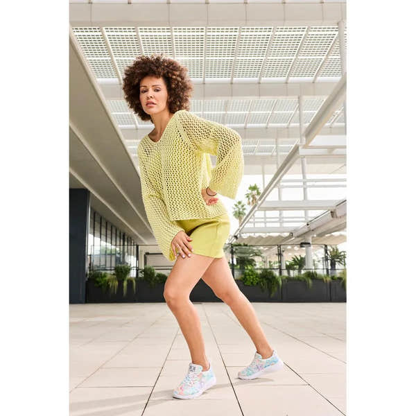 Rieker M8500-90 vegan lace-up trainers in multi-colored textile, worn by a woman in a yellow outfit, set in a modern indoor space.