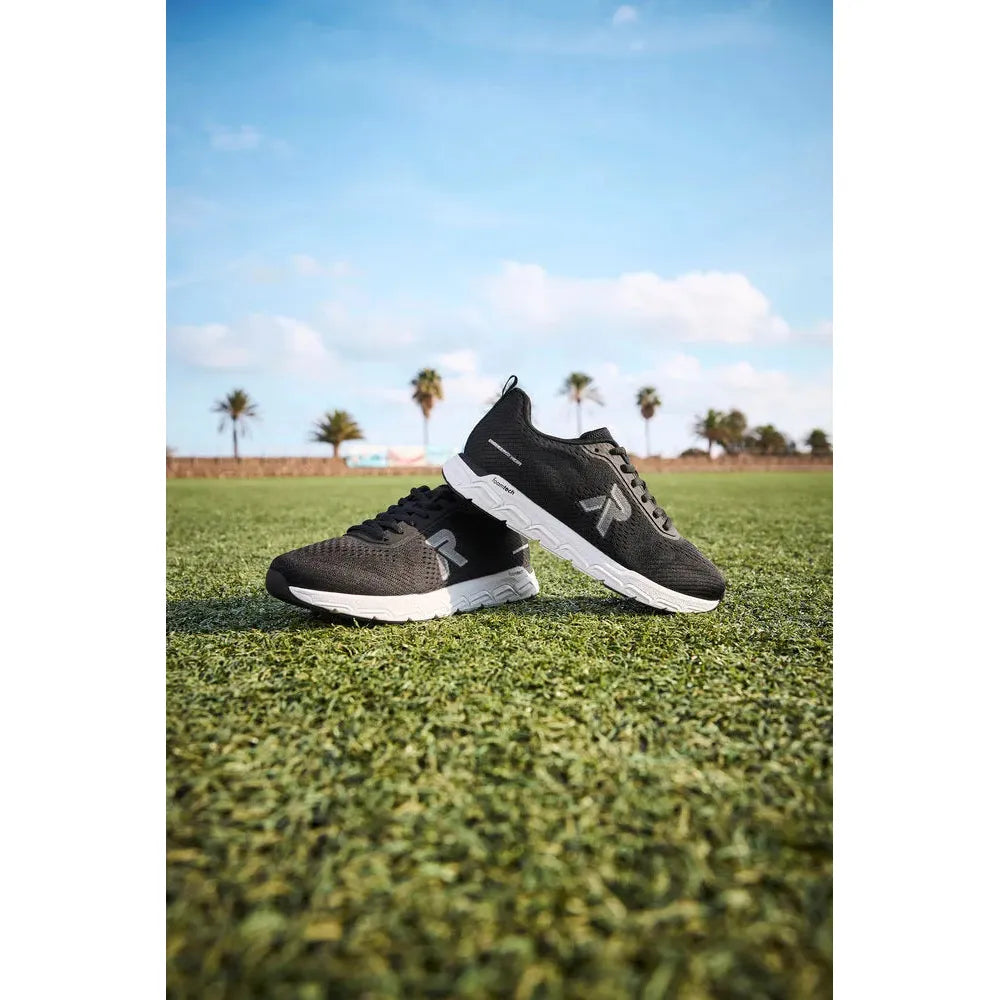 Rieker M9006-00 women's wide-fit black textile lace-up trainers on grassy field with palm trees in background.