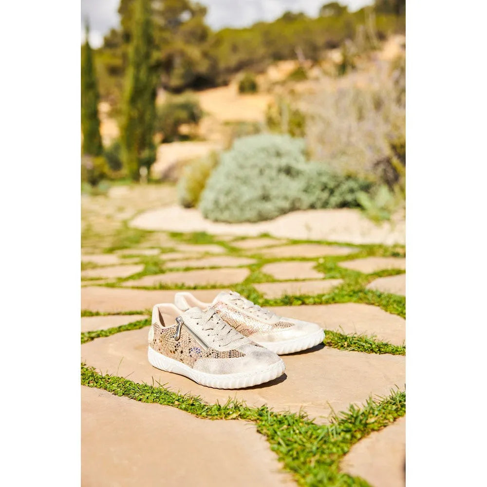 Rieker N0902-90 women's multi-zip and lace casual shoes with metallic accents, worn on a stone pathway with greenery.