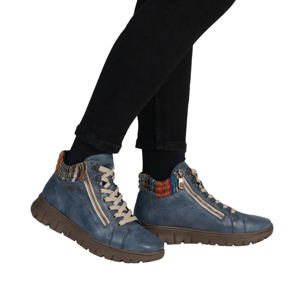 Rieker N1305-14 women's blue leather ankle boots with zip, lace-up, and colorful knit collar, on black pants.