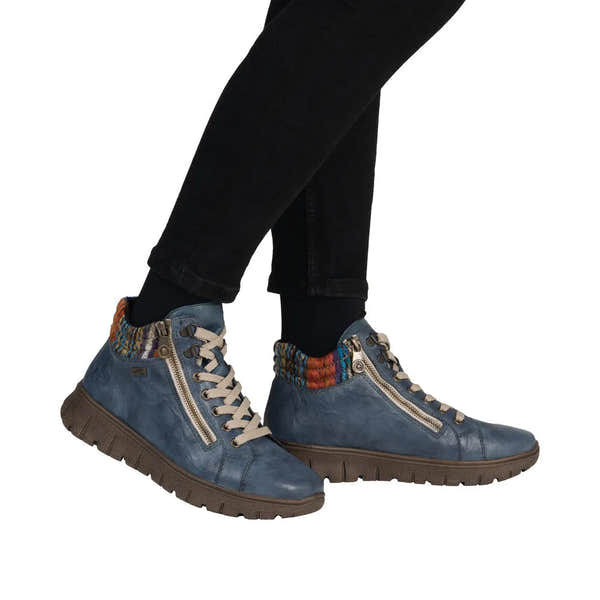 Rieker N1305-14 women's blue leather ankle boots with zip, lace-up, and colorful knit collar, on black pants.