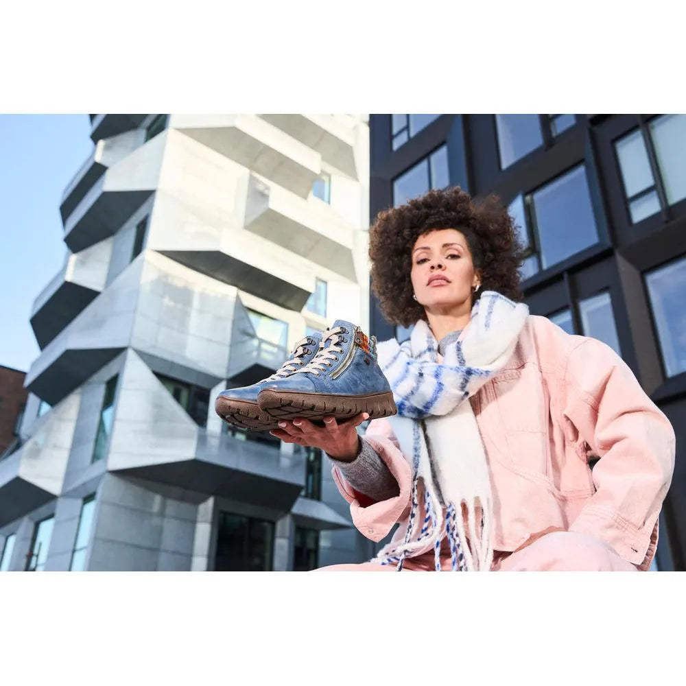 Rieker N1305-14 women's blue leather ankle boots with zip and lace detail, featuring a rugged sole, urban backdrop.