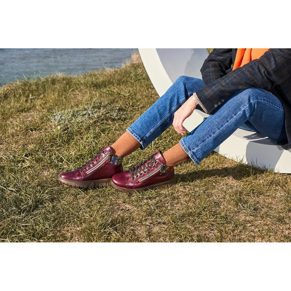 Rieker N1305-35 women's red leather ankle boots with zip and lace-up design, mid-high heel, worn with blue jeans and brown socks outdoors.