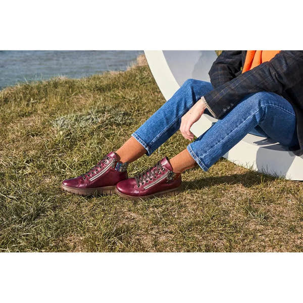 Rieker N1305-35 women's red leather ankle boots with zip and lace-up design, mid-high heel, worn with blue jeans and brown socks outdoors.