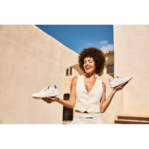 Woman holding white Rieker N1313-80 wide leather trainers with zip and lace-up design, outdoor sunny setting.
