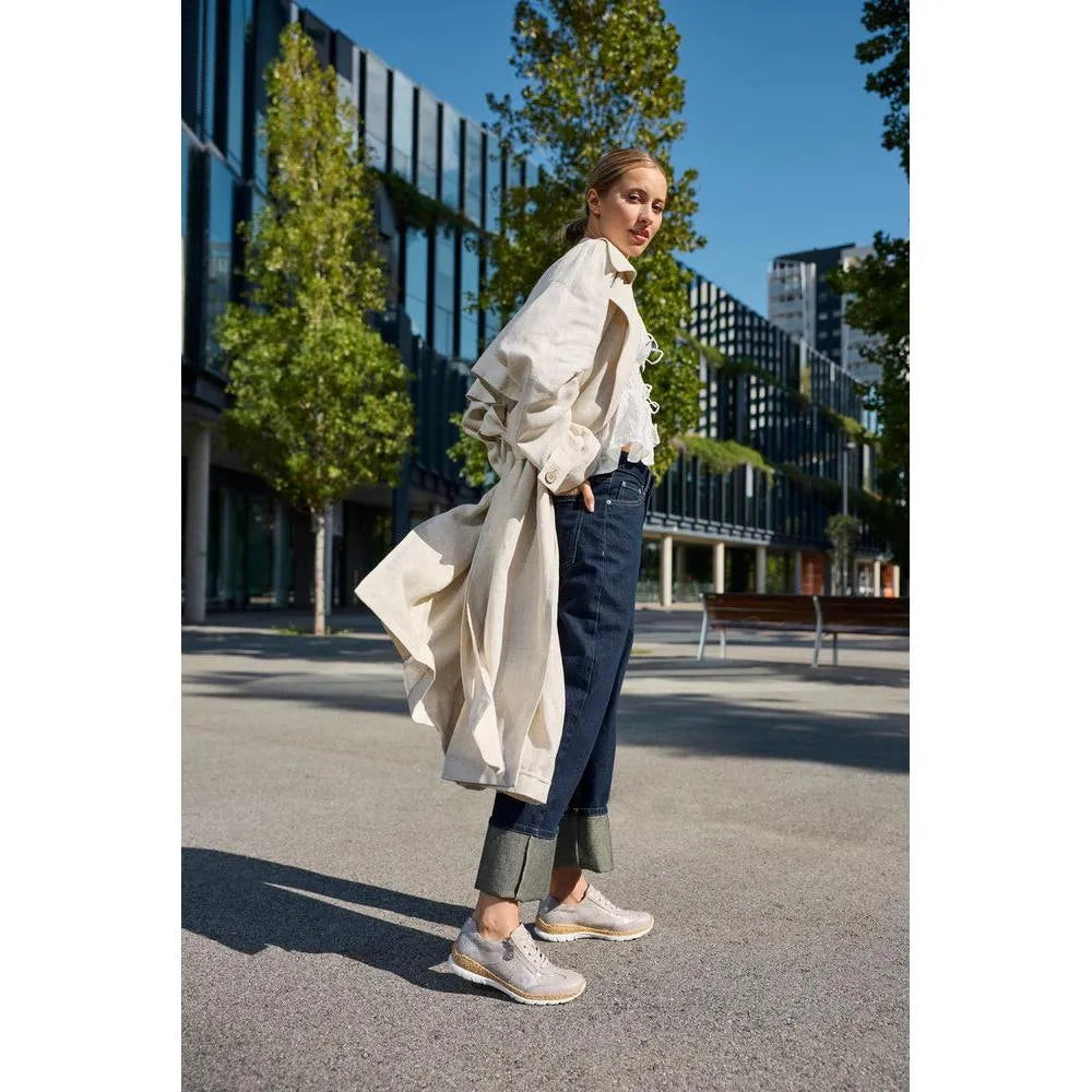 Lady wearing beige metallic zip and lace shoes, dark cuffed jeans, and a light oversized trench coat outdoors.