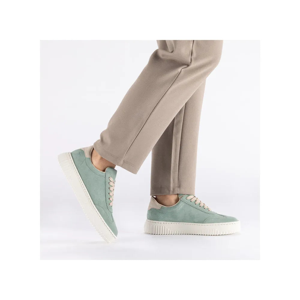 Mint suede lace-up trainers with cream sole and beige accents, worn with beige trousers.