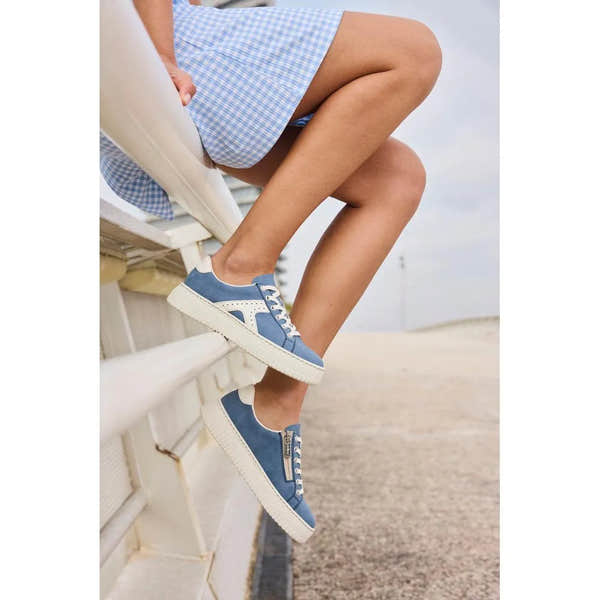 Light blue and off-white lace and zip trainers with a cushioned white sole, worn by a woman sitting on a beachside bench.