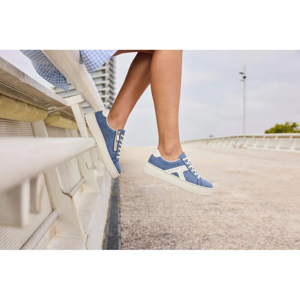 Light blue and off-white lace and zip trainers with素材 and sporty style, worn by a person sitting on a bench outdoors.