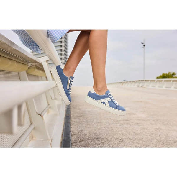 Light blue and off-white lace and zip trainers with素材 and sporty style, worn by a person sitting on a bench outdoors.
