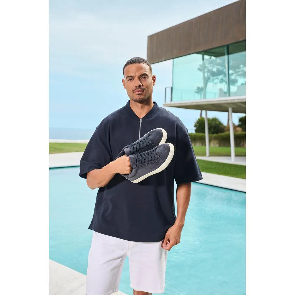 Men's blue suede lace-up shoes with white soles, styled casually against a modern outdoor backdrop.